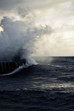 a large wave crashing into the ocean on top of a boat in front of it