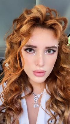 a woman with long curly hair and blue eyes wearing a white shirt is looking at the camera