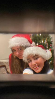 two women in santa hats are looking at the camera