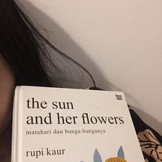 a woman holding up a book about the sun and her flowers by rupi kaur