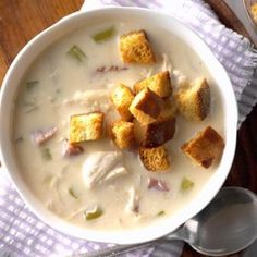 a white bowl filled with soup and croutons on top of a wooden table