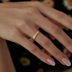 a woman's hand with pink and white manicured nails holding a gold ring