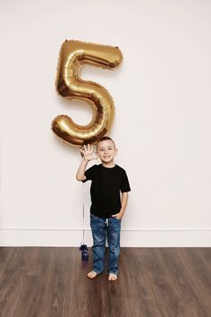 a young boy standing in front of a number five balloon