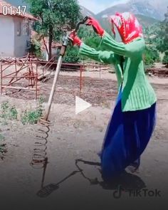 a woman in blue pants and green sweater holding a metal pole with red flowers on it