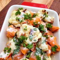 a white dish filled with cauliflower and carrots on top of a wooden table