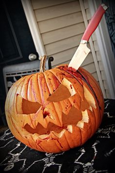 a carved pumpkin with a knife sticking out of it's mouth on top of a table