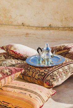 a glass tea pot sitting on top of a pillow next to pillows and a tray