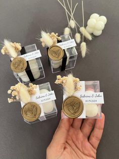 four small clear boxes with waxed labels and dried flowers in them, one being held by a person's hand