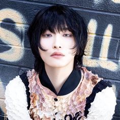 a woman with black hair and moustaches standing in front of a graffiti covered wall