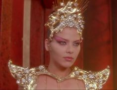 a woman in a gold costume with wings and jewels on her head is staring at the camera