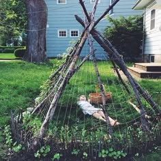 a person laying on the ground in front of a teepee with some branches attached to it