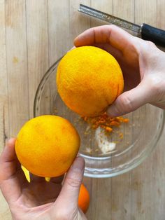 two hands holding oranges in front of a glass bowl filled with spices and seasoning