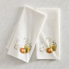 two white towels with pumpkins on them sitting on a marble counter top next to each other