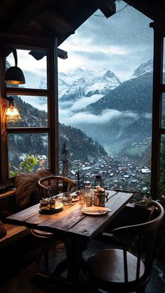 a wooden table sitting in front of a window covered in snow next to a mountain