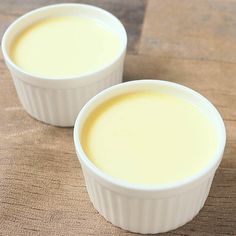 two small white bowls filled with cream on top of a wooden table