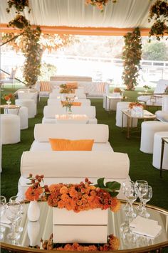 an outdoor event with white couches, orange flowers and candles on the side tables