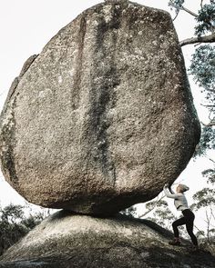 a person climbing up the side of a large rock with trees in the back ground