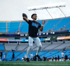 a man holding a football on top of a field in front of an empty stadium