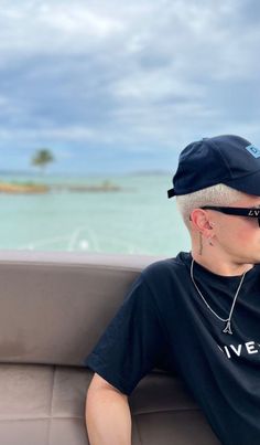 a man sitting on top of a boat next to the ocean wearing sunglasses and a hat