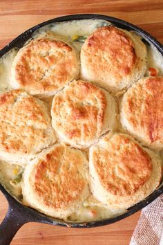 some biscuits are cooking in a skillet on a wooden table with a white towel