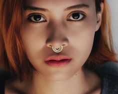 a woman with red hair wearing a nose ring and piercing on it's nose