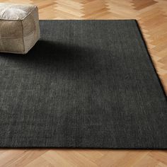 a black area rug on top of a wooden floor next to a chair and ottoman