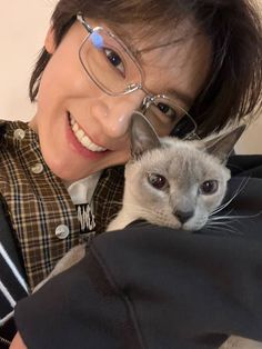 a woman holding a cat in her arms and smiling at the camera while wearing glasses