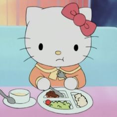 a hello kitty sitting at a table with food in front of her and a spoon