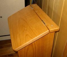 a wooden toilet seat sitting on top of a hard wood floor next to a refrigerator