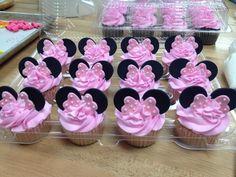 cupcakes with pink frosting and minnie mouse ears on them are displayed in plastic trays