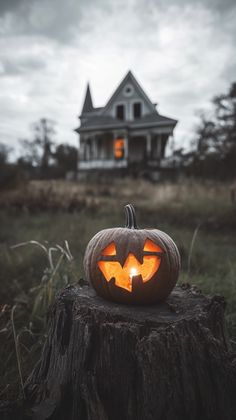 a carved pumpkin sitting on top of a tree stump in front of a creepy house