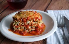 a white plate topped with lasagna covered in sauce next to a glass of wine