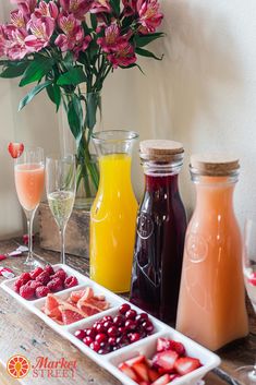 a table topped with drinks and fruit next to vases filled with flowers on top of a wooden table