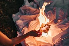 a person is holding a card in their hand while sitting on the ground next to a fire