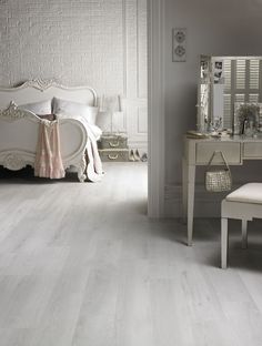 a bedroom with white walls and flooring has a bed, chair, dresser and mirror