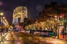 a city street at night with cars parked on the side of the road and lights on