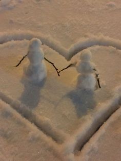 two snowmen standing in the shape of a heart on top of snow covered ground