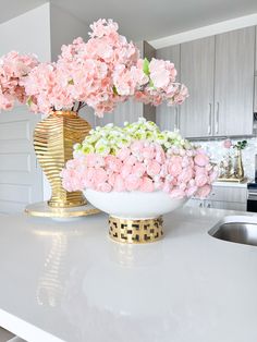 pink flowers are in a gold vase on the kitchen counter