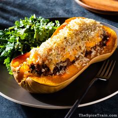 a black plate topped with a stuffed sweet potato next to greens and a fork on a blue table cloth