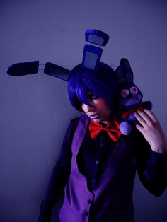 a woman with blue hair wearing a purple suit and red bow tie holding a stuffed animal in front of her head