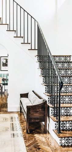 a white staircase with black railing and wooden bench in the center, along with patterned rugs