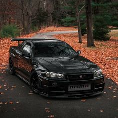 a black car parked on the side of a road in front of trees and leaves