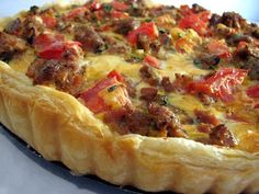 a quiche with meat and tomatoes on it sitting on a counter top, ready to be eaten