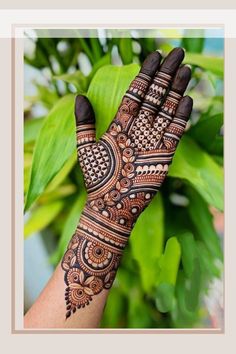 a woman's hand with henna tattoos on it and green leaves in the background