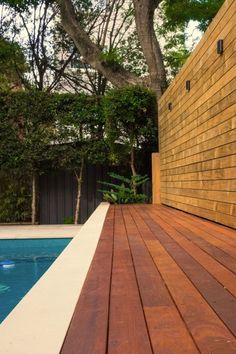 a wooden deck next to a swimming pool in a backyard with trees and shrubbery