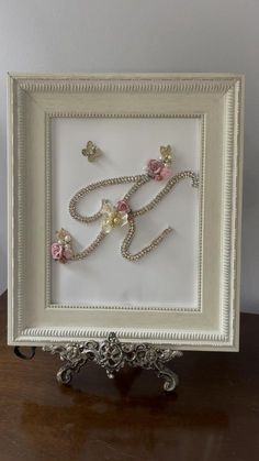 a white frame with beads and flowers in the shape of an e on top of a wooden table