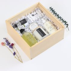 an open wooden box containing soaps and body care products on a white surface next to flowers