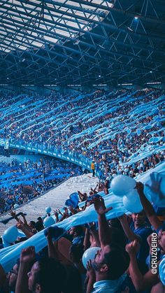 many people are sitting in the bleachers and holding up their blue scarfs