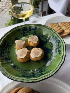 three small pastries on a green plate next to a glass of wine and some crackers