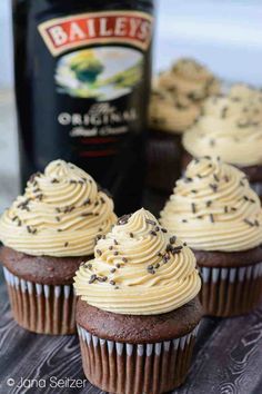 three chocolate cupcakes with frosting and sprinkles next to a bottle of bailey's